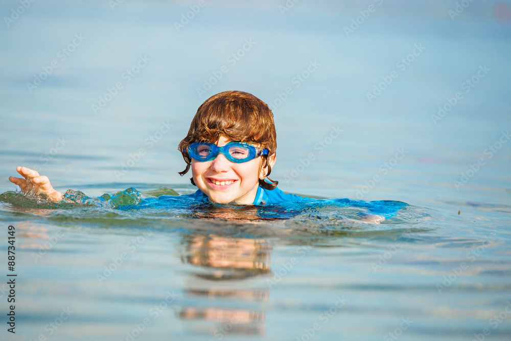 Happy smiling boy with goggles on swim in shallow water
