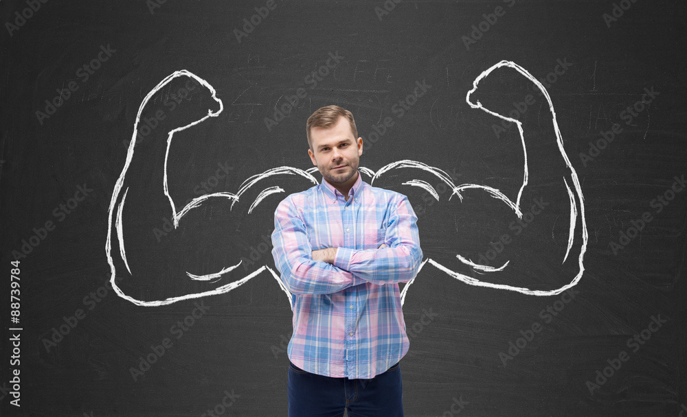 Young handsome man in casual shirt with drawn powerful hands. Black chalkboard background.