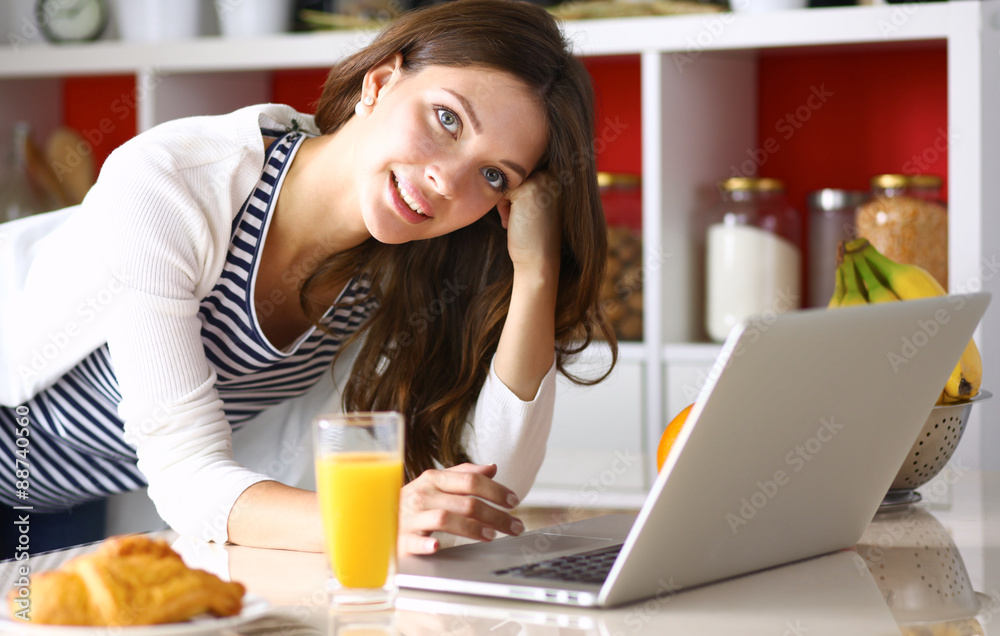 Attractive young woman using laptop and sitting in the kitchen Attractive young woman using laptop and sitting in the kitchen