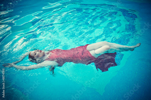 Young sexy woman floating on swimming pool in red dress. beauty shot