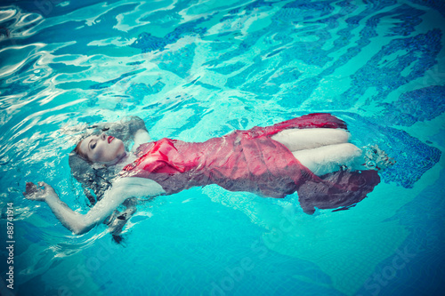 Young sexy woman floating on swimming pool in red dress. beauty shot