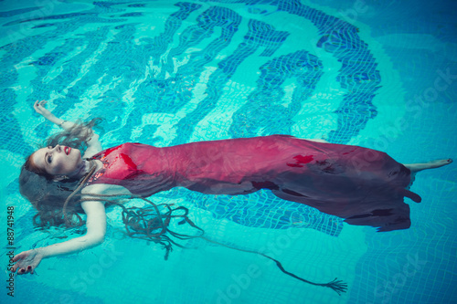 Young sexy woman floating on swimming pool in red dress. beauty shot