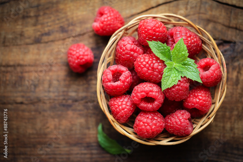 Fresh ripe red raspberries in a wicjer bowl on dark rustic wooden background