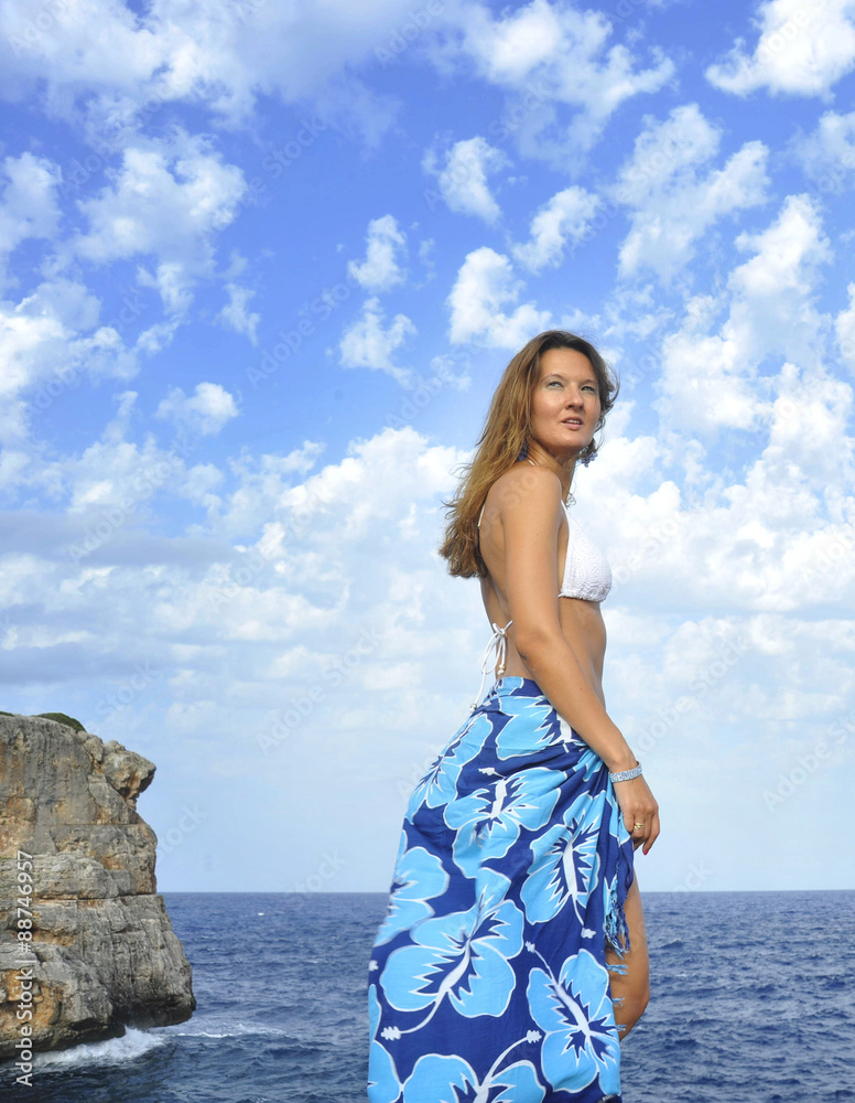 woman looking at ocean horizon on rock cliff by sea shore in sarong beach wrap