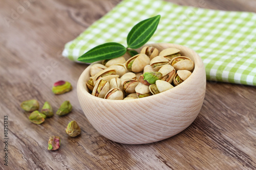 Pistachio nuts in wooden bowl on checkered cloth 