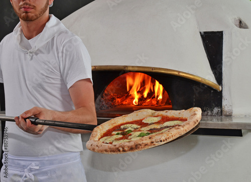 Cocinero panadero cocinando una piza en un horno a leña  photo