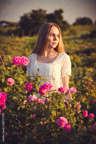 Beautiful woman in garden with roses at sunset