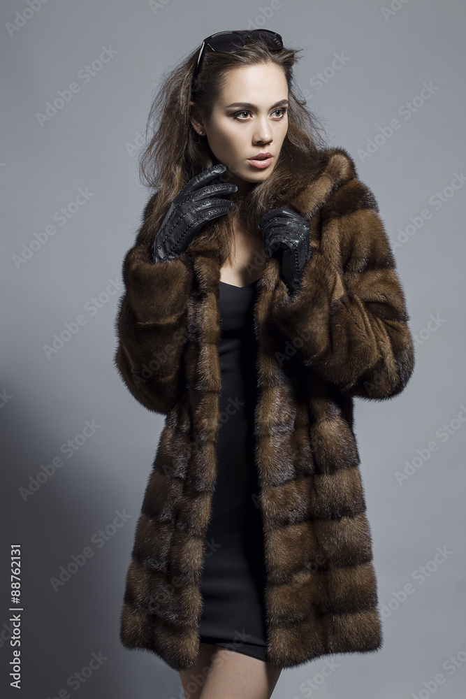 Sexy Beauty Girl with natural Make up. Fashion Brunette Portrait of a girl dressed in fur coat, black dress and sunglasses posing on a grey background. Retro style Sexy Beauty Girl with natural Make up. Fashion Brunette Portrait of a girl dressed in fur coat, black dress and sunglasses posing on a grey background. Retro style