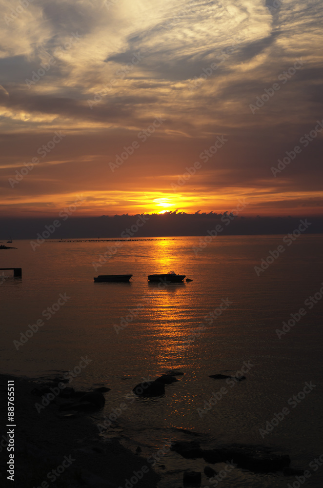 beautiful sunset at seaside with silhouette of boats vertically cropped
