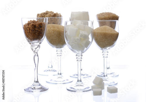Different types of sugar in glasses on white.