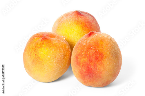 Three ripe peach with drops of water on a white background