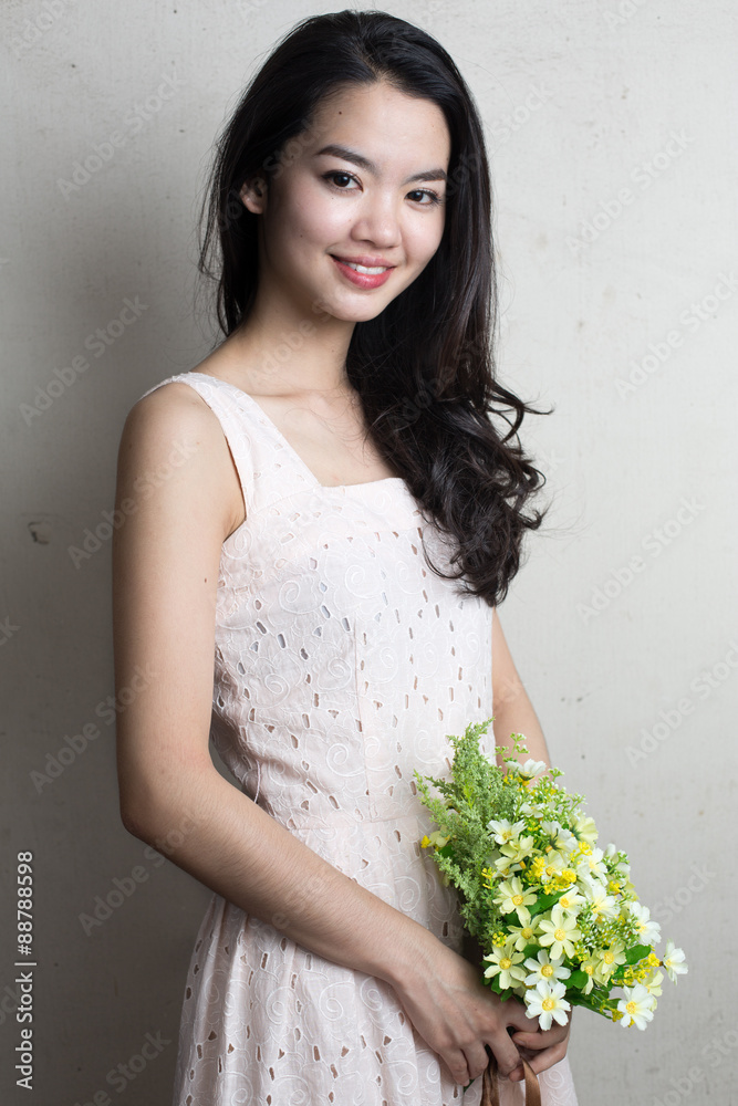 Asian lady holding a bunch of flower standing against a wall Asian lady holding a bunch of flower standing against a wall