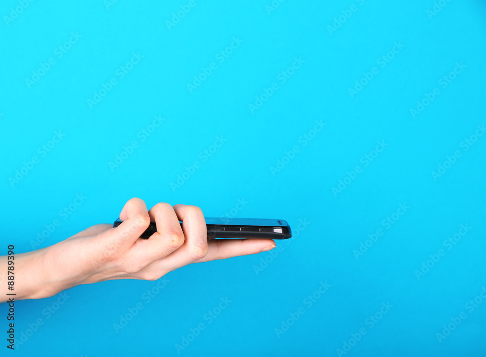 Female hand using mobile phone on blue background Female hand using mobile phone on blue background