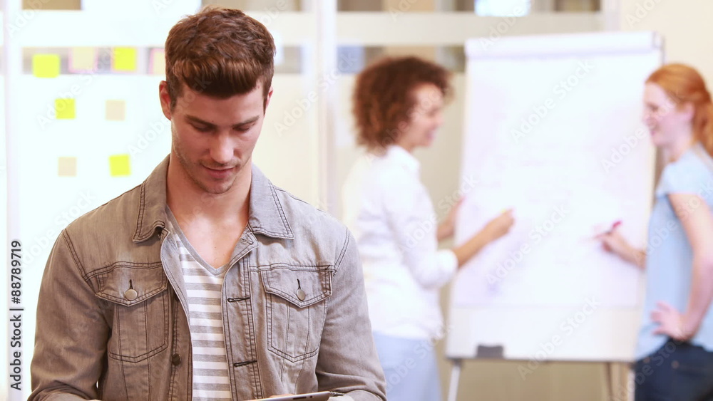 Casual businessman using tablet in front of colleagues Casual businessman using tablet in front of colleagues