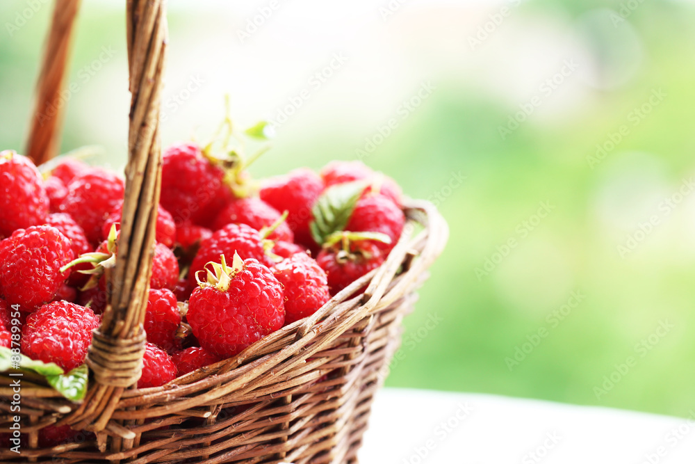 Fresh raspberries in wicker basket on wooden table on blurred nature background Fresh raspberries in wicker basket on wooden table on blurred nature background