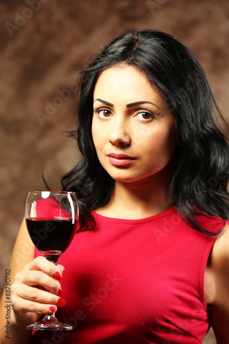 Pretty young woman with wineglass on brown background