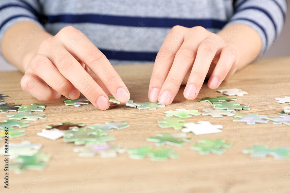 Female hands assembling puzzle on wooden table, closeup Female hands assembling puzzle on wooden table, closeup