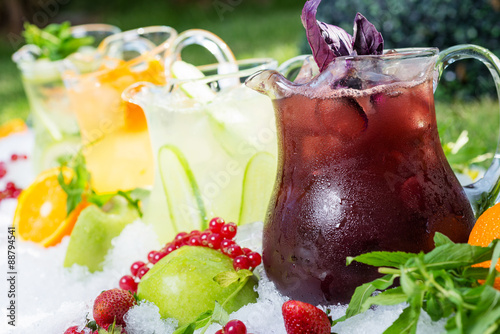 a mix of several bright colored delicious cold lemonade carafes of cucumber and orange and basilon with creative composition photo