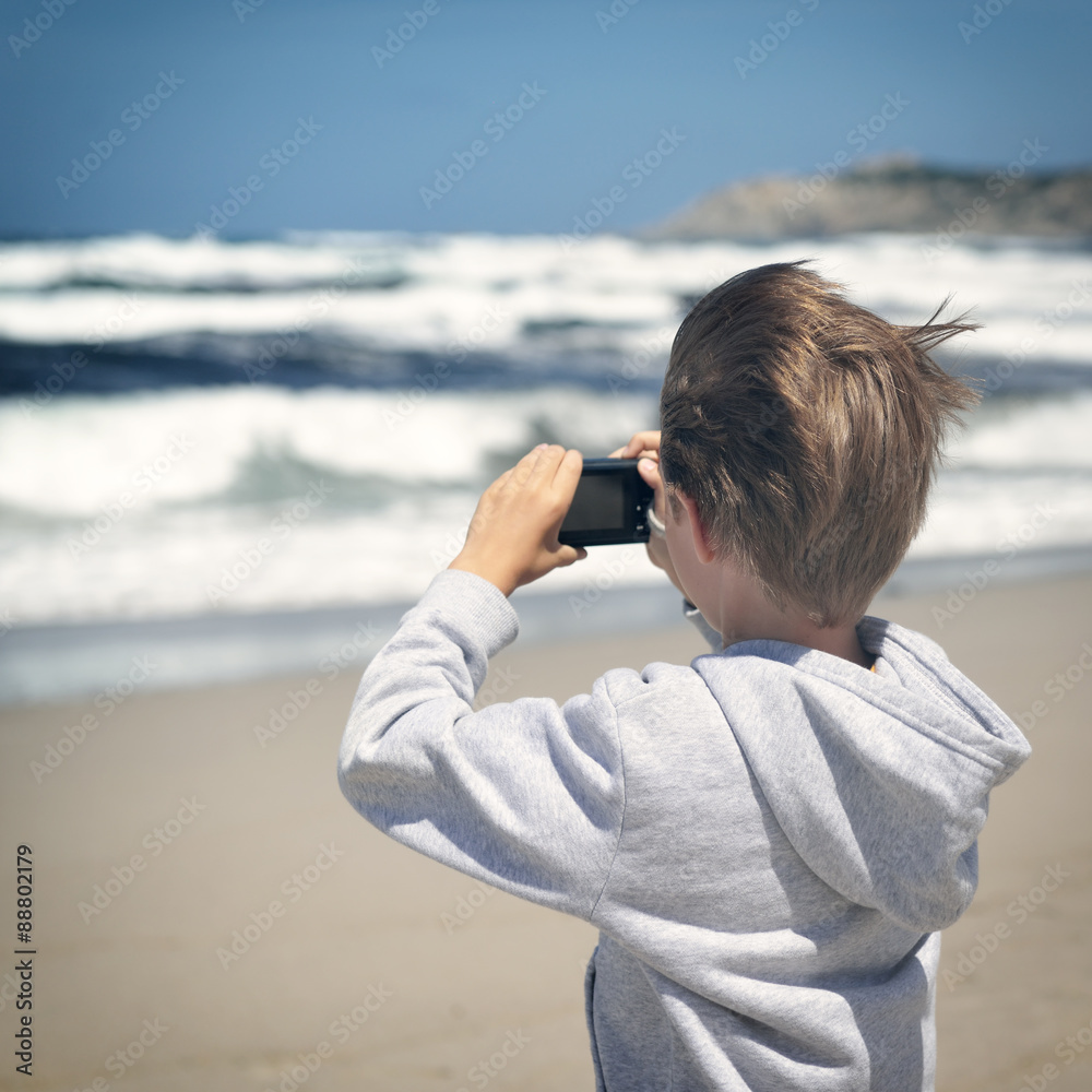 young boy makes photos with photo camera on the sea coast, toned
