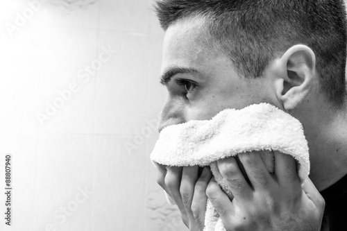 Handsome young man is drying his face with towel looking at the mirror photo