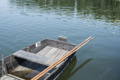 Fragment of traditional wooden fishing boat with oars attached in still water of river