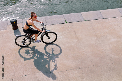 Canvas Print Young woman riding a bike on the stone embankment of the river