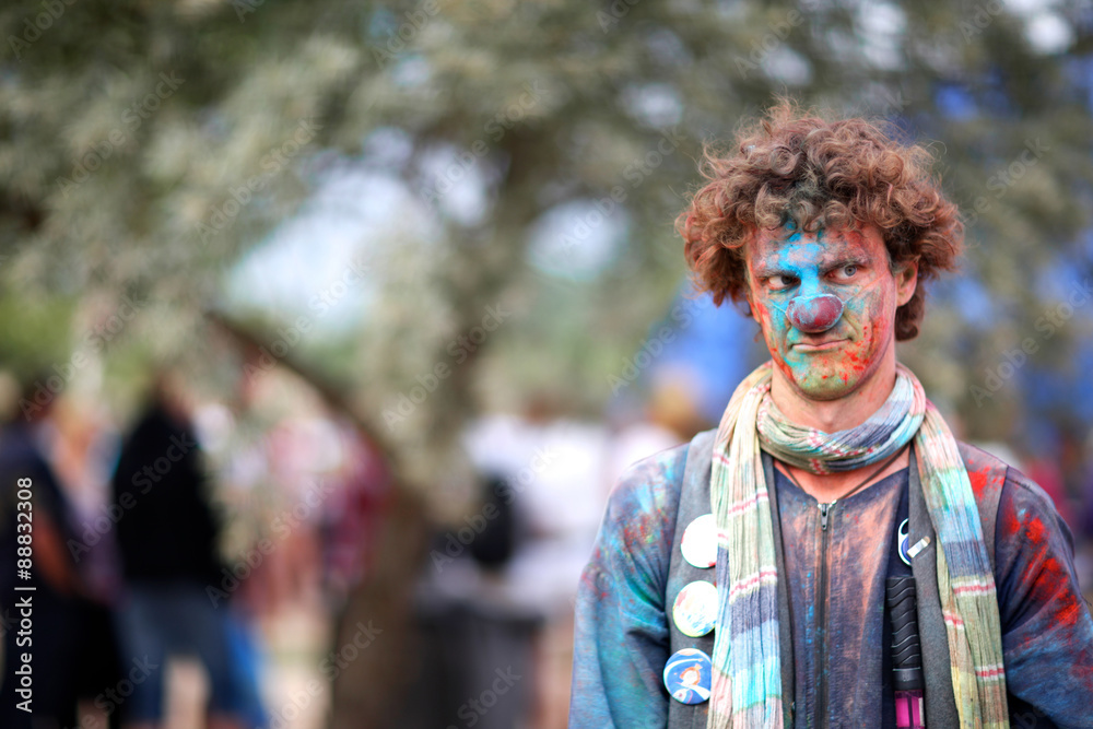 Curly clown covered with colored powder thoughtfully looking aside