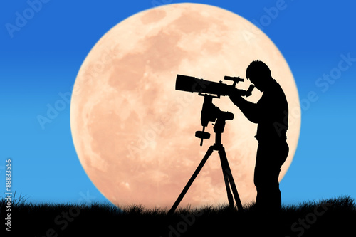 silhouette of young man looking through a telescope at the full