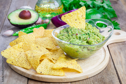 Bowl with chunky guacamole served with nachos and ingredients on backgroung