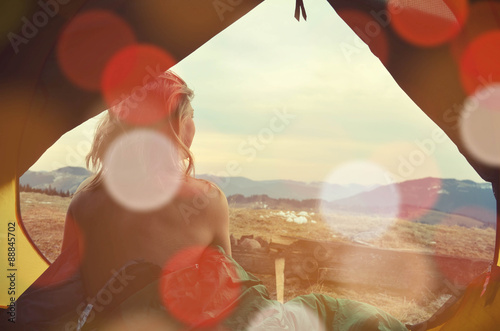 A young woman sitting in the tent with naked back, looking at th
