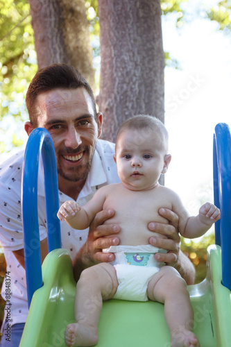 Bebe en brazos de su padre jugando en el parque. Primer plano de un padre jugando con su bebe desnudo en pañal. Bebe feliz. photo