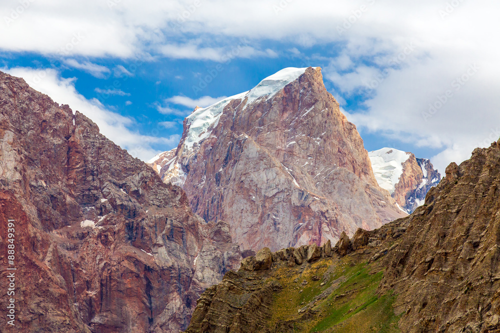 Mountain terrain panorama. Bright landscape of Fan Mountains in Tajikistan with mixed layer of colors green meadow on foreground brown rocks in middle red peaks with glaciers and snow on background
