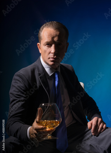 The man is sitting with a glass of whiskey