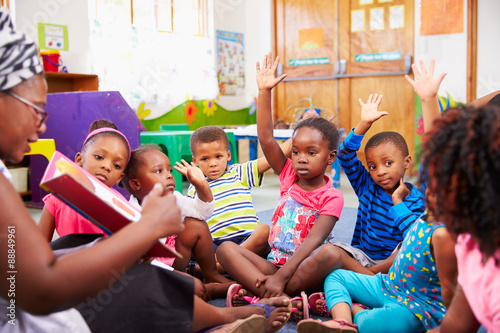 Class of preschool children raising hands to answer teacher