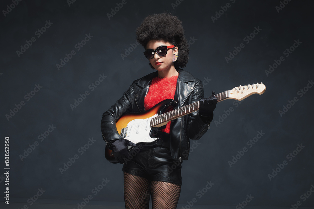 Fototapeta premium Rocker Girl Holding a Guitar Against Black Wall
