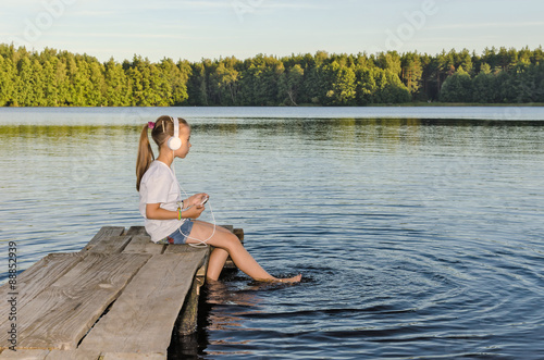 ГАРМОНИЯ/
Девочка слушает музыку сидя на деревянном мостике на озере. 