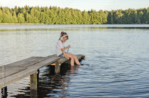 ГАРМОНИЯ/ Девочка слушает музыку сидя на деревянном мостике на озере. 