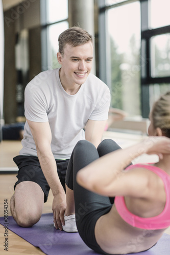 smiling woman with male trainer exercising in gym