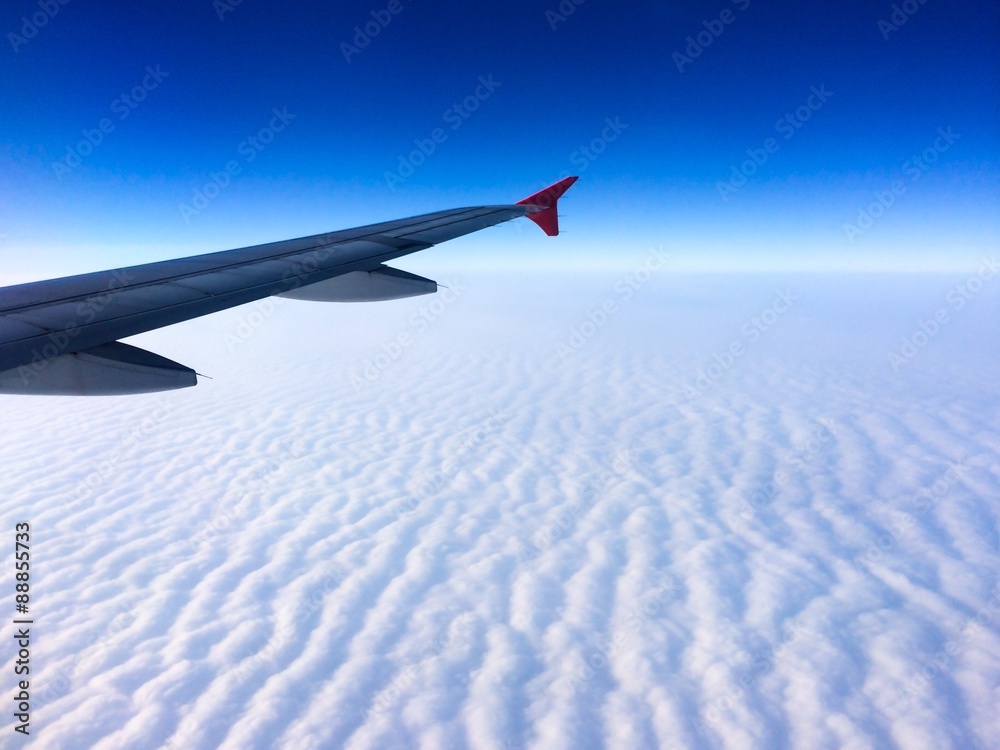 Obraz premium Wing of the plane with cloudy sky on background