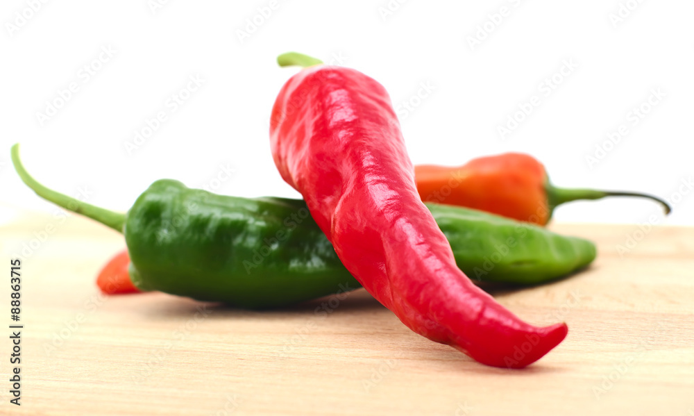 Colorful pepper pods closeup on wooden surface, white background, local soft focus, shallow DOF.  