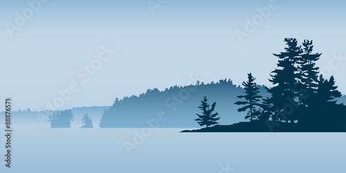 Misty silhouette of the landscape of a northern lake with pine forest and isalnds.