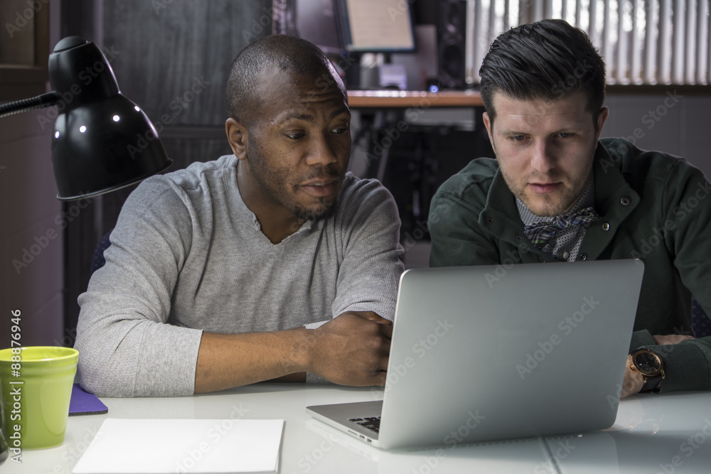 African American and Caucasian man using a laptop in the office African American and Caucasian man using a laptop in the office