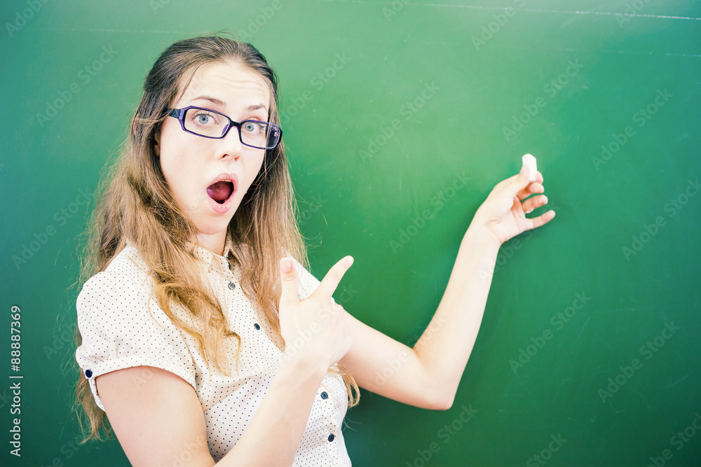 Happy young teacher or student is pointing at blackboard background Happy young teacher or student is pointing at blackboard background