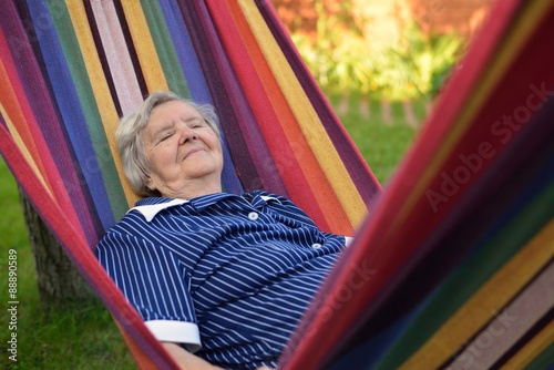 Senior happy woman resting on a hammock in garden.