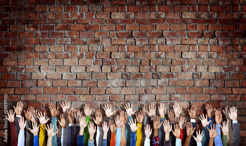 Group of Diverse Hands Raised on Brick Wall photo