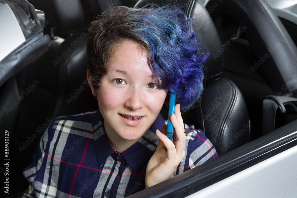 Smiling teenage girl seating in car while talking on cell phone