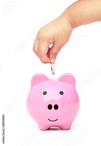 baby hand putting a golden coins into a pink piggy bank with piles of golden coins arranged as a graph - saving money for security in life concept