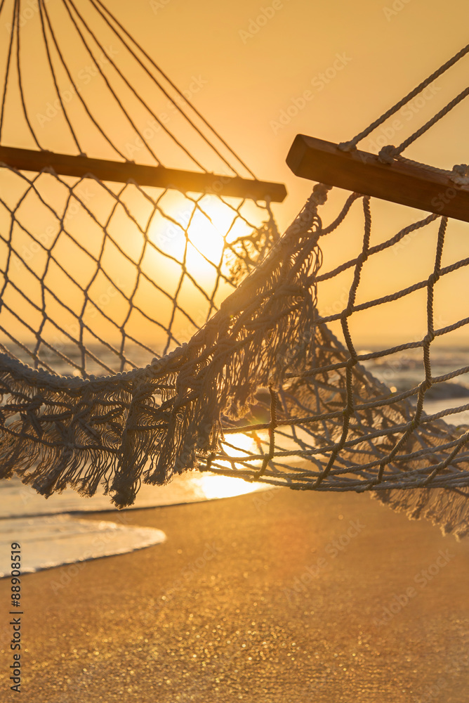 hammock on sandy beach overlooking ocean at bright sunset