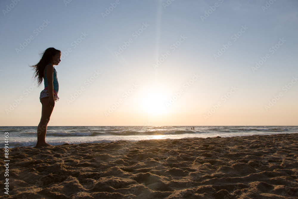 Bambina in piedi di profilo sulla spiaggi in controluce