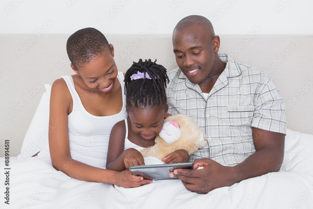 Fototapeta premium Pretty couple using tablet with their daughter in bed